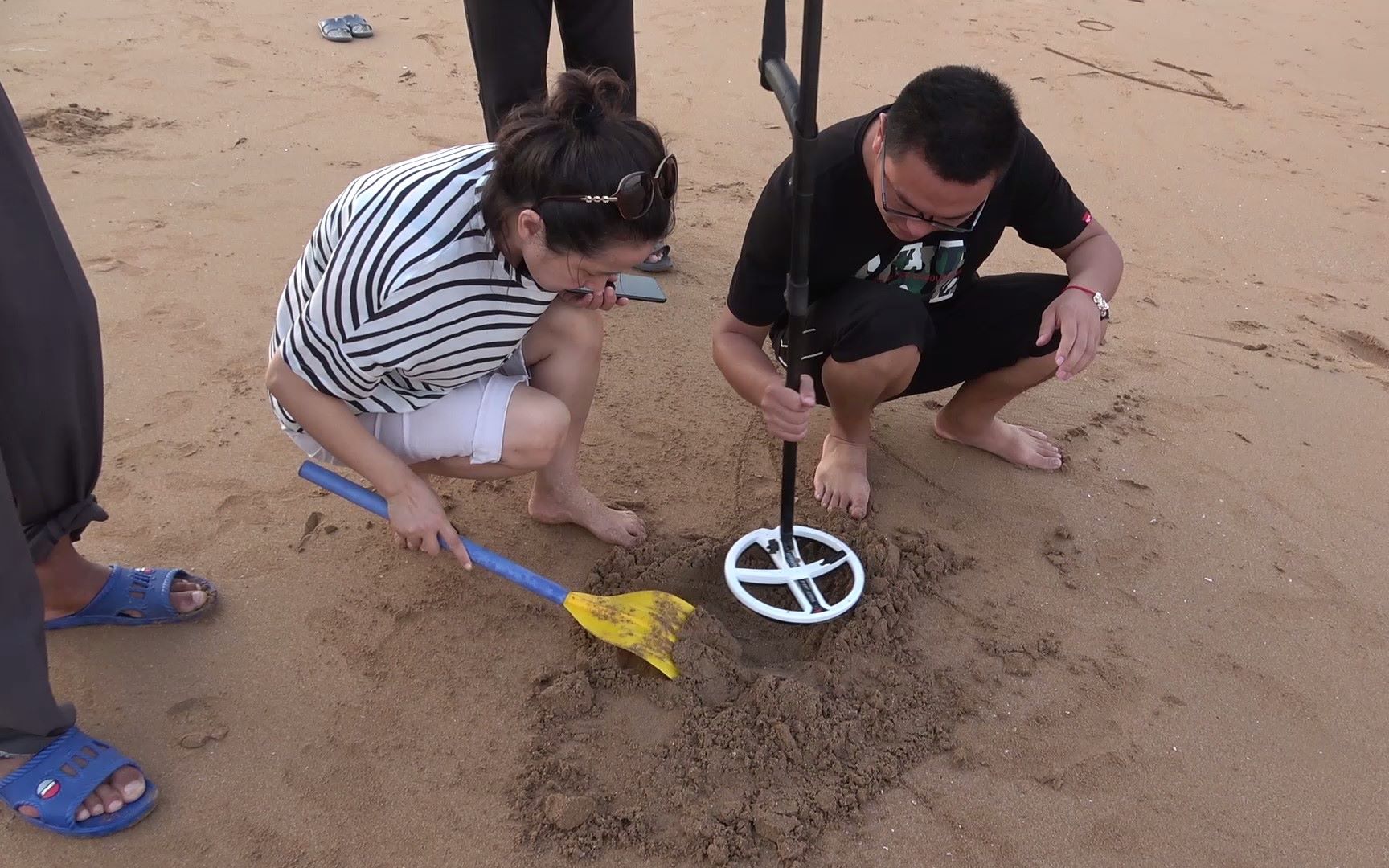 拿着金属探测器在海滩探宝挖出的东西引一群人围观