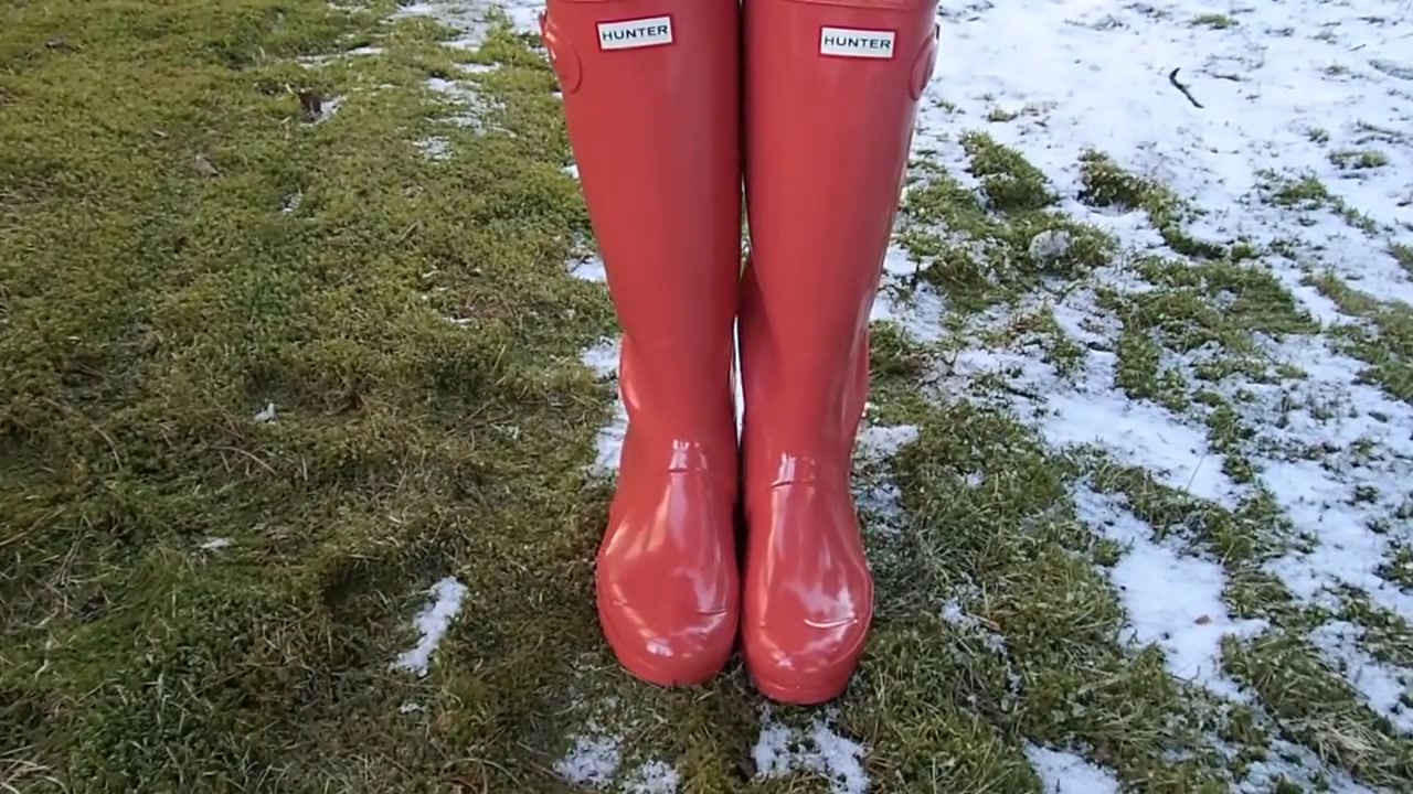 冰雪草地上穿橘红色亮面高筒hunter雨靴